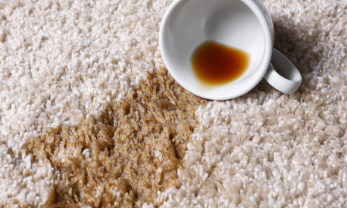 A cup of spilled tea creating a brown stain on a rug