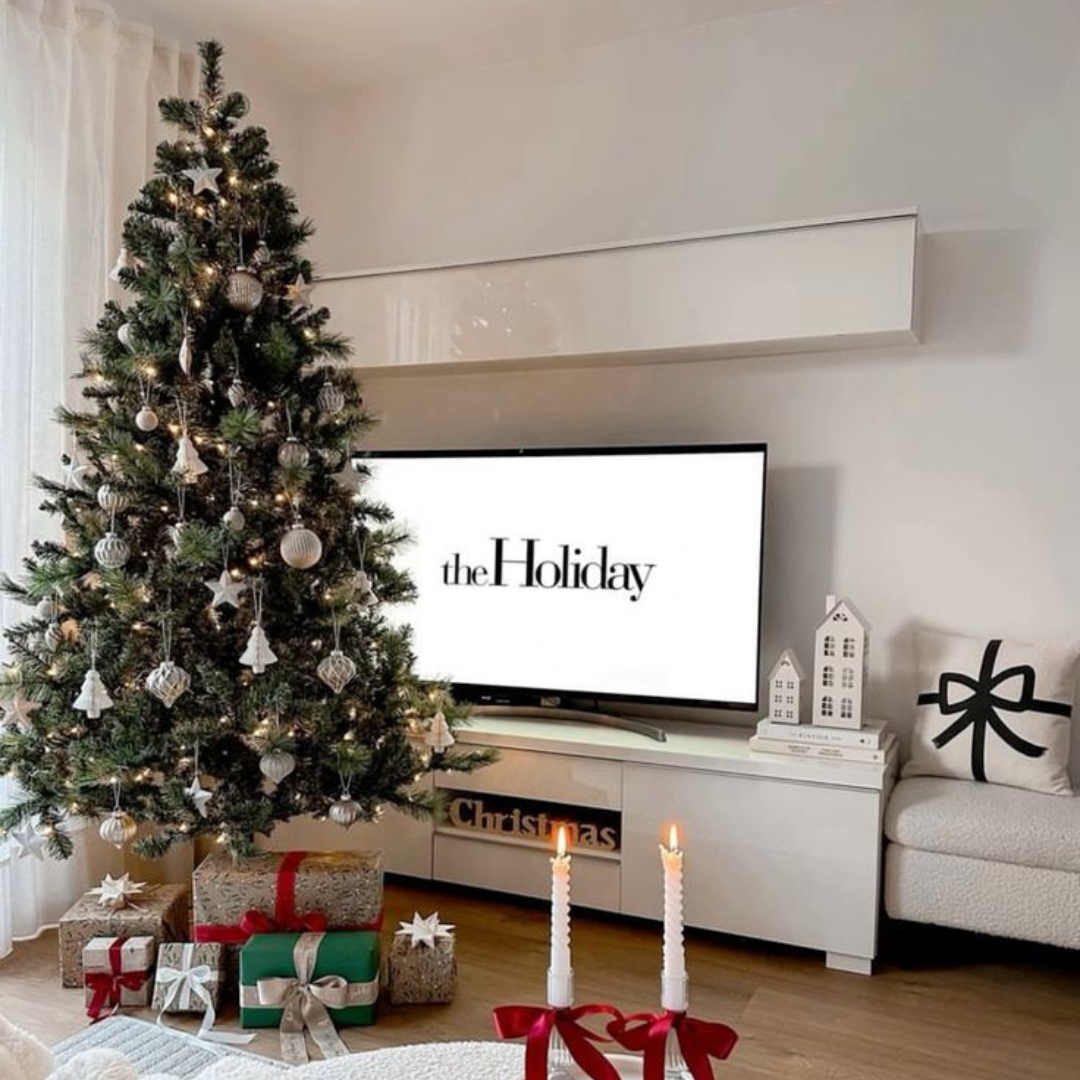 A festive Christmas tree stands in front of a TV, with a pile of wrapped presents scattered on the floor below.