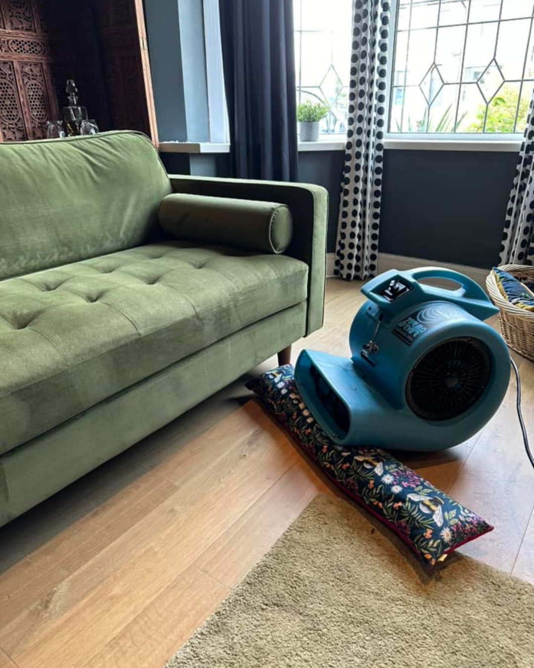 A blue air blower placed on the floor, speeding up the drying process after sofa cleaning.