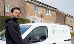 Man in a black hoodie stands beside a white van with "enviroclean" logo, in front of a suburban house. The scene conveys professionalism and readiness.