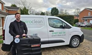 A person in a black hoodie stands smiling next to a carpet cleaning machine in front of a van with "enviroclean" branding, conveying professionalism.