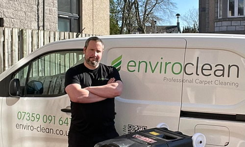A person stands confidently with arms crossed in front of a white van labeled "enviroclean" for carpet cleaning, conveying professionalism.