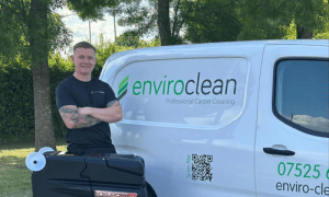 A man stands smiling beside a white van with "enviroclean" branding, parked outdoors. The atmosphere is professional and friendly.
