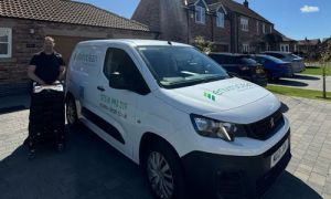 Man standing next to a white van with "Enviroclean" branding, parked on a residential street. Sunlit brick houses are visible in the background.