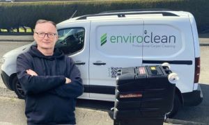 A person stands confidently with arms crossed, in front of a white van labeled "enviroclean Professional Carpet Cleaning." A cleaning machine is nearby.