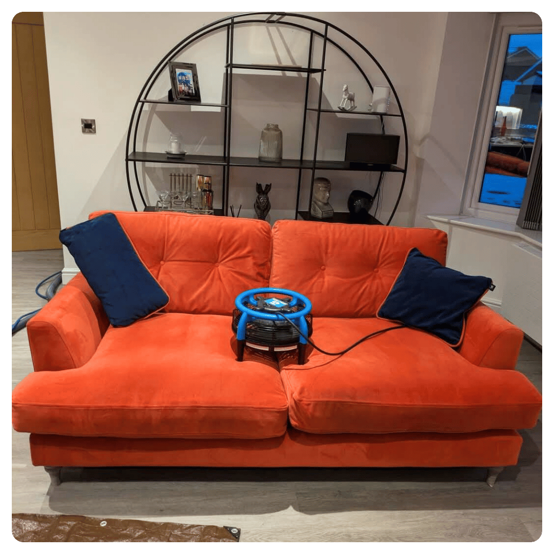 Orange sofa with two dark blue pillows beside a circular black metal shelf with decor.