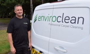 Approachable professional man in a black tshirt, infront on a branded "enviroclean" van.