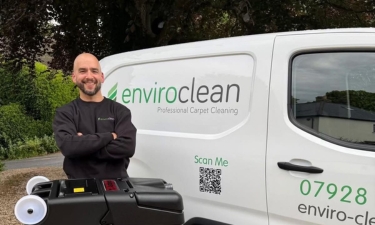 Person smiling, standing next to carpet cleaning machine, in front of a white van labeled "enviroclean." The scene conveys professionalism and expertise.