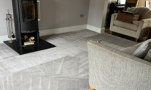 A cozy living room with a modern fireplace, neatly vacuumed carpet, and comfortable beige sofas. The ambiance is warm and inviting.