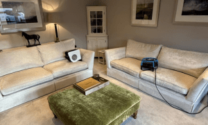 Beige sofas and a green footstall, with drying equipment on, after being freshly cleaned by enviro clean.