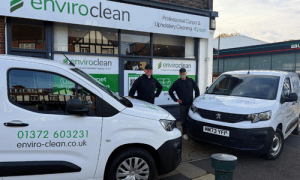Two men in uniform standing in front of the shopfront, with branded 'enviro clean' vans
