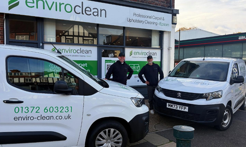Two men in uniform standing in front of the shopfront, with branded 'enviro clean' vans
